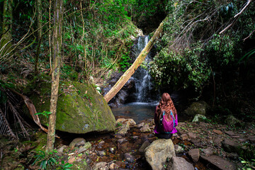 backpacker girl relaxing in front of hidden tropical waterfall in australian rainforest; warrie circuit in springbrook national park near gold coast, queenslan