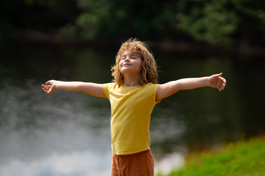 Happy kid with arms up enjoying freedom in nature. Kid enjoying freedom raising arms up. Funny happy little boy having fun at the park. Kid enjoy summer, childhood. Kid in nature.