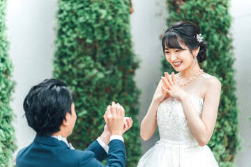 プロポーズで指輪・エンゲージリングをプレゼントされるウェディングドレスを着た笑顔のアジア人女性・新婦
