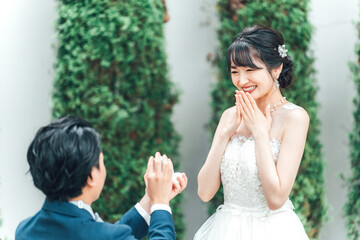 プロポーズで指輪・エンゲージリングをプレゼントされるウェディングドレスを着た笑顔のアジア人女性・新婦
