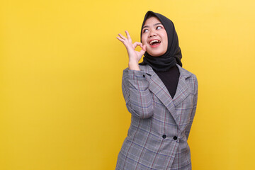 Smiling happy millennial Muslim girl isolated on yellow studio background show OK sign, happy...