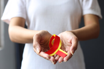Close-up shot of female hands holding red yellow ribbon to support patient with hepatic disease....