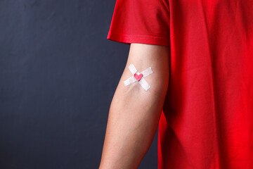 Blood donor in red t shirt with bandage after giving blood on a grey background. Blood donation and...