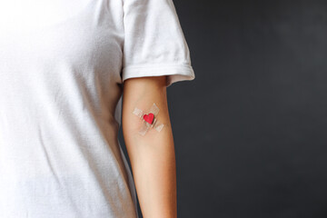 Partial view of woman blood donor in white t-shirt with plaster heart. Blood Donation Concept