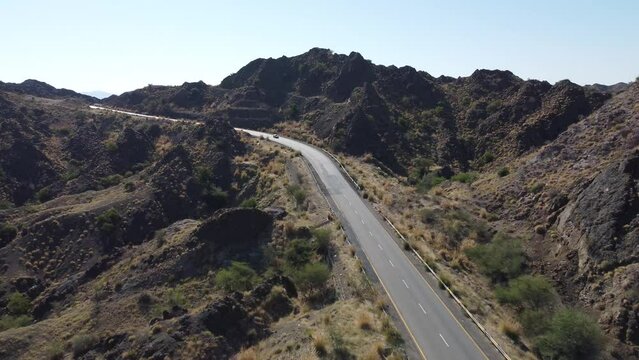 Aerial drone view of a car racing down a lonely highway in the desert mountains of Balochistan