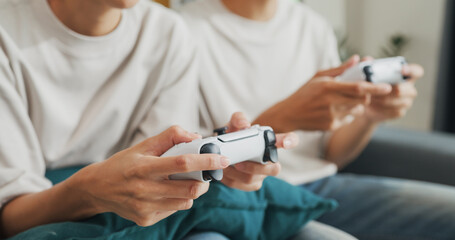 Close-up Young Asian couple sit on couch hold joystick play video game spend time together have fun at home on weekend. Happy husband and wife laugh relax with online game, Lifestyle activity concept. © tirachard