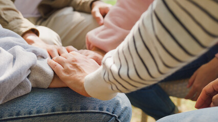 Close-up of diverse multiracial men and women group sit in circle hold hands together hope for help people in park. Support and understand at psychological therapy session, PTSD Mental health concept.