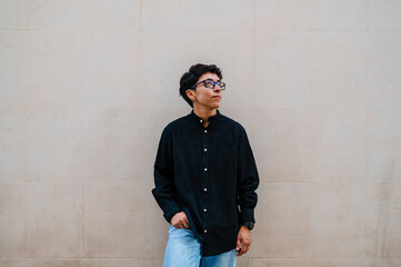 Young transgender man leaning on a wall while posing outdoors on the street.