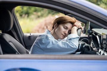 Middle aged tired woman sleeping on steering wheel exhausted from long driving in road trip. Female driver feels fatigue resting having break on highway. Traveling by car, journey on long distance.