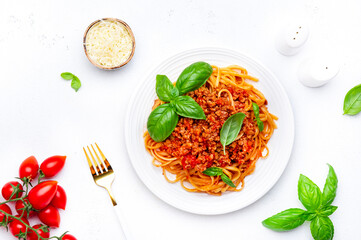 Spaghetti bolognese or pasta with minced meat in tomato sauce with green basil, white table background, top view