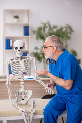 Old male doctor examining skeleton in the clinic