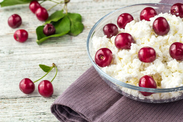 Breakfast from cottage cheese with cherry in transparent bowl on white wooden background