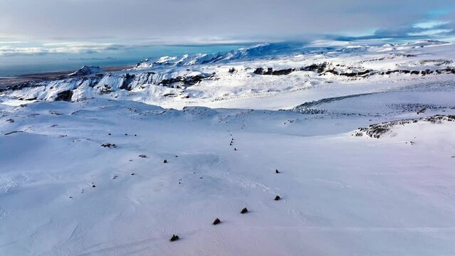 Aerial panoramic landscape view of people riding snowmobiles on the frozen ground of Myrdalsjokull glacier in Iceland, at dusk