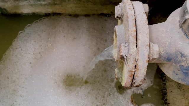 Dirty waste water coming out from pipe on Wastewater Treatment Procedure (WWTP). Pouring water produce foam on the pond. Chemical waste water from industrial process.