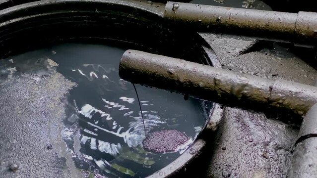 Black chemical wastewater pouring on the storage tank coming out from pipe from industrial processes on WWTP Wastewater Treatment Procedure. Hazardous and toxic waste water. Water mixed with oil
