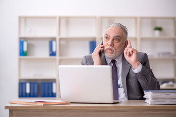 Old male employee speaking by phone at workplace
