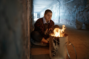 Lonely woman beggar warming hands by fire at night in tunnel