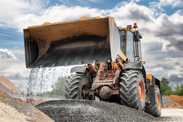 Powerful wheel loader or bulldozer on sky background. Loader pours crushed stone or gravel from the bucket. Powerful modern equipment for earthworks and bulk handling. © Anoo