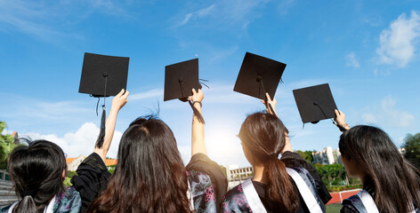 Rear view of four female graduates holding their hats  in the air