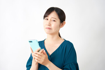 スマートフォンを持って悩む女性　白背景　カメラ目線