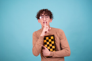 Mind games. An attractive guy in a brown sweater poses with chess on a blue background.