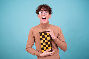 Mind games. An attractive guy in a brown sweater poses with chess on a blue background.