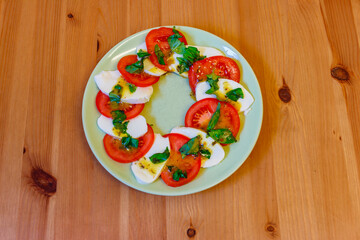 Italian caprese salad with tomatoes, mozzarella cheese and basil on a wooden table. Top view