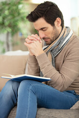 man on sofa holding book his hands in prayer position