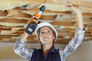 female construction worker using cordless drill on wooden ceiling joists