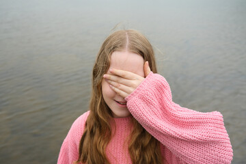 Little girl covering eyes with hand near river