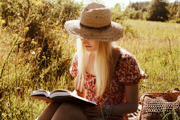 Young blonde woman in a straw hat with a book in the summer