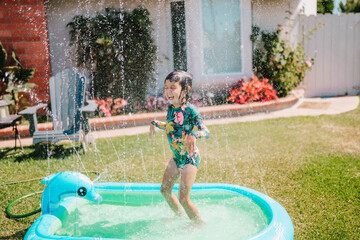 Toddler Girl Playing In Yard With Sprinkler