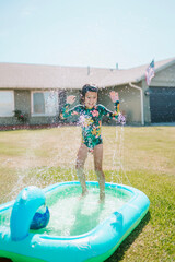 Toddler Girl Playing In Pool In Yard With Sprinklers