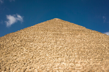 Fototapeta na wymiar Closeup detail one side of Pyramid of Khufu or the Pyramid of Cheops against blue sky with some clouds and small moon, Giza, Egypt