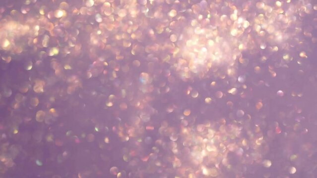 Abstract motion of gold bokeh lights on purple background. Blurry gold particles in liquid float and glisten. Defocused sparkling golden bokeh circles wavy movement in 4K resolution.