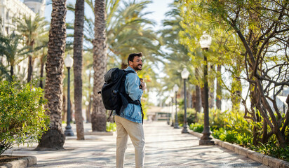 A traveler with backpack is walking on the tropical street during his vacation in Spain.