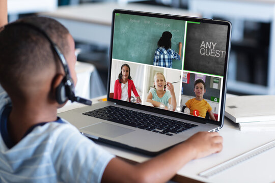 African american boy in headphones and looking at teacher and students during online class on laptop