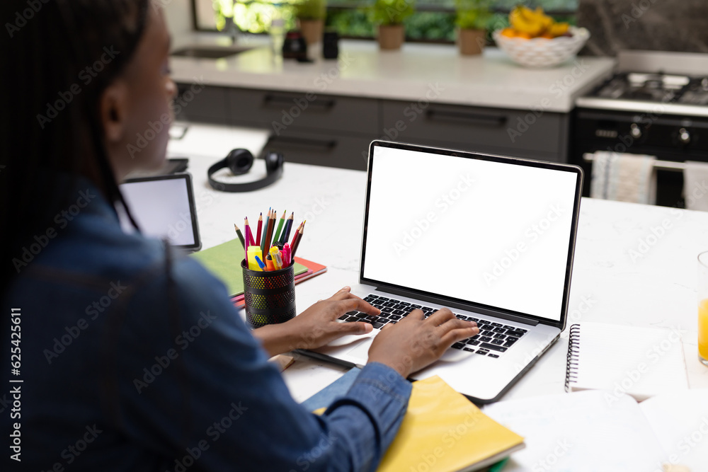 Wall mural African american teenage girl studying online over laptop on table at home, copy space