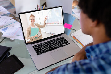 African american boy looking at female teacher teaching over video call on laptop screen