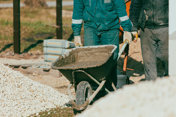 Workers are carrying a wheelbarrow with sand and cement