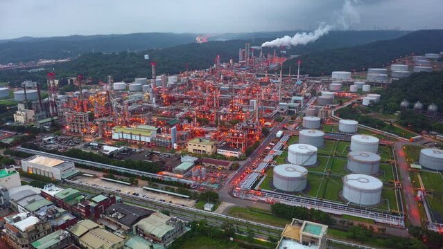 Aerial hyperlapse over a CPC oil refinery plant in a petrochemical industrial estate, with huge storage tanks and pipelines throughout the factory and the lights glowing at dusk in Taoyuan, Taiwan