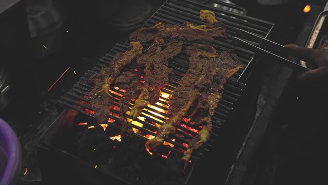 Closeup of a man grilling marinated raw meat or beef slices on a charcoal grill