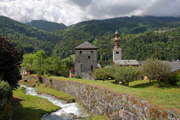 The church of Saint Francois de Sales and the Tour de Bozel (Bozel tower), located in the commune Bozel, Northern French Alps, Tarentaise, Savoie, France, with the mountain stream Le Bonrieu  