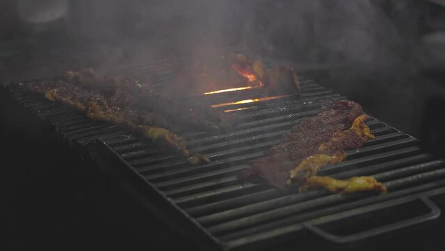 Closeup of a man grilling marinated raw meat or beef slices on a charcoal grill