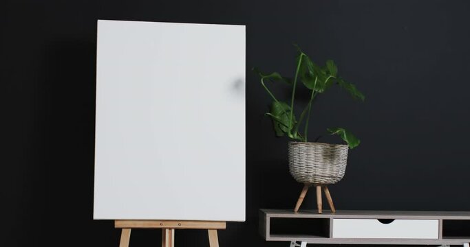 Video of white canvas sign on wooden easel with copy space and plant on desk on black background