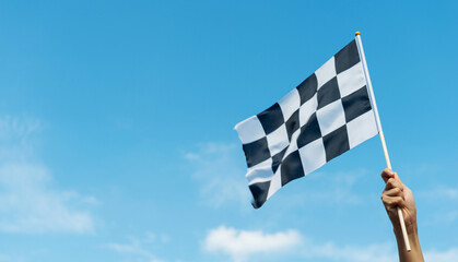 Checkered race flag in hand against blue sky