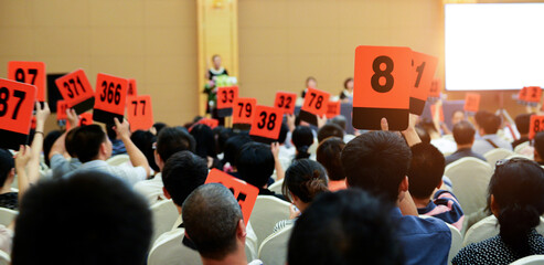 Crowd of bidders holding their numbered bidding paddles at an auction - obrazy, fototapety, plakaty