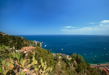 Photograph of the coast of Taormina in Sicily, houses, boats and trees.