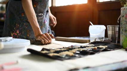 Pottery artist in apron kneading piece of raw clay on wooden table. Handicraft, creativity, hobby and activity concept