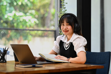 Online education, e-learning. Happy Asian young woman wearing headphone, studying remotely, using a laptop